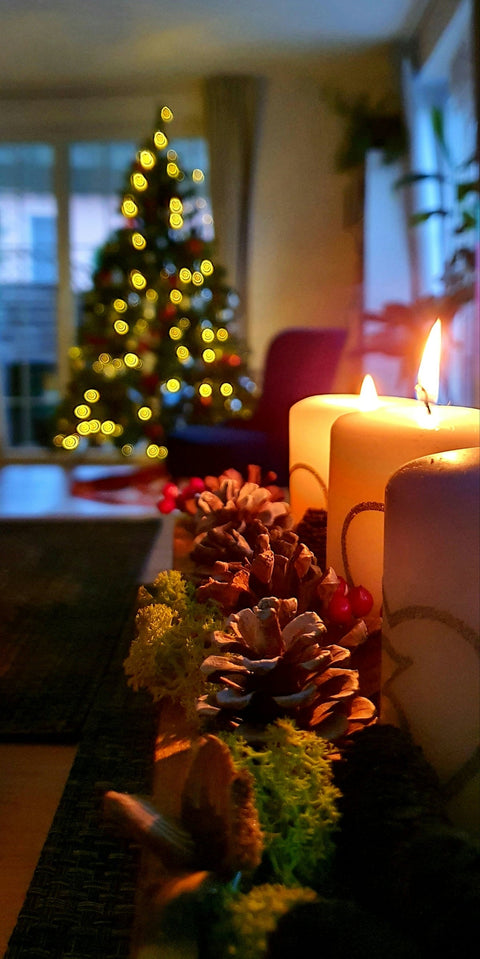 two candles are sitting on a table with a christmas tree in the background