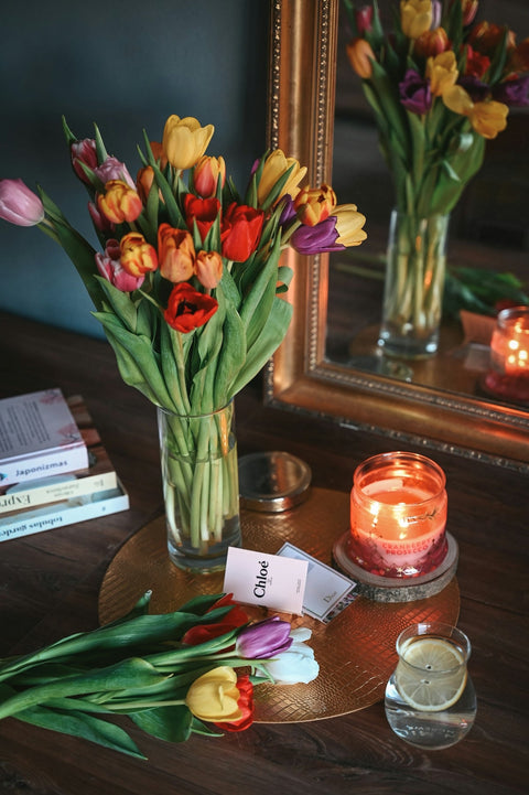 Colorful tulips in vase with lit candle and mirror.